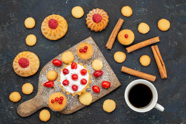 Vista dall'alto piccole torte gustose con crema di caffè alla cannella e frutta fresca sulla bacca di frutta dolce del dessert della torta del biscotto della scrivania scura