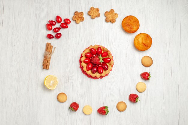 Vista dall'alto piccoli biscotti con frutta e torta sulla scrivania bianca