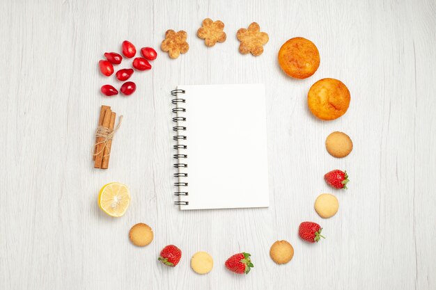 Vista dall'alto piccoli biscotti con frutta sulla scrivania bianca