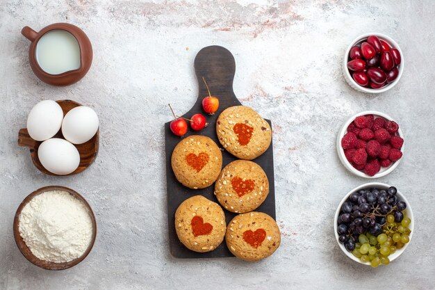 Vista dall'alto piccoli biscotti di zucchero deliziosi dolci per tè con frutti di bosco sulla superficie bianca torta biscotto zucchero torta dolce