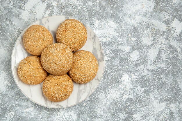 Vista dall'alto piccoli biscotti morbidi deliziosi dessert per il tè all'interno del piatto su superficie bianca