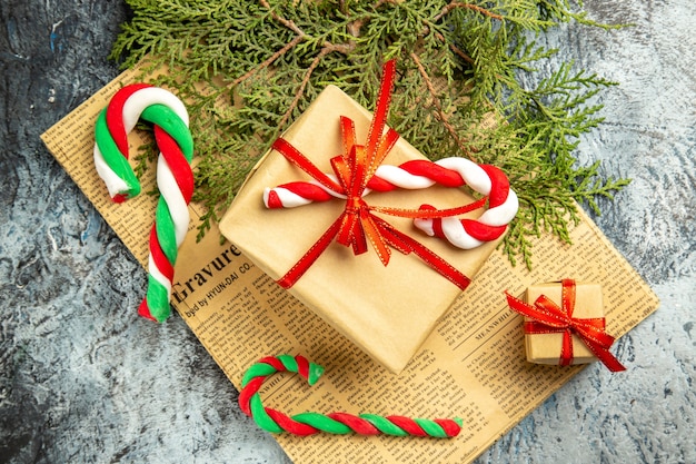 Vista dall'alto piccoli regali legati con nastro rosso caramelle natalizie su giornali su superficie grigia