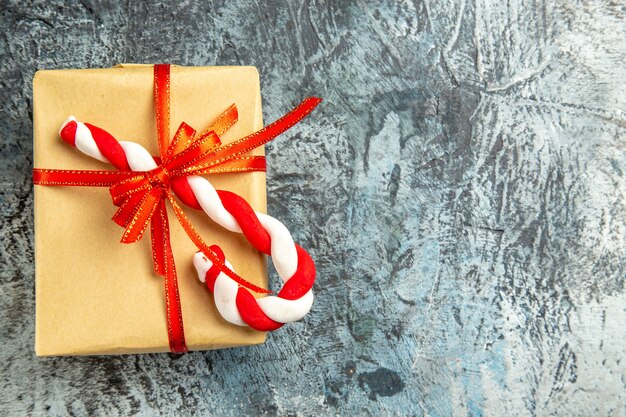 Vista dall'alto piccolo regalo legato con nastro rosso caramelle natalizie su sfondo grigio spazio copia