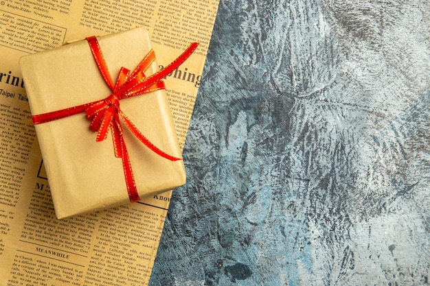 Vista dall'alto piccolo regalo legato con nastro rosso su giornale su superficie scura