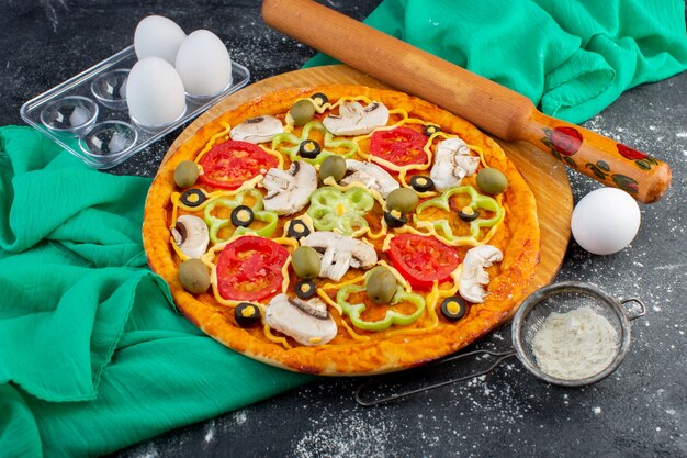 Vista dall'alto pizza ai funghi con pomodori olive funghi tutti affettati all'interno con uova sulla scrivania grigia pasta per pizza tessuto verde cibo italiano