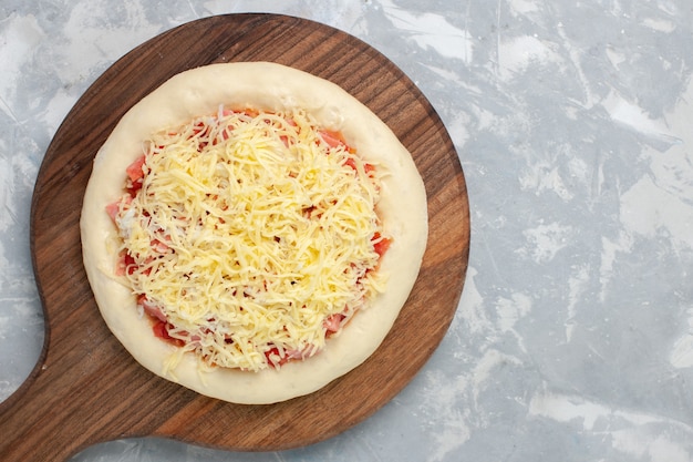 Vista dall'alto pizza cruda con formaggio prima di andare in forno su bianco