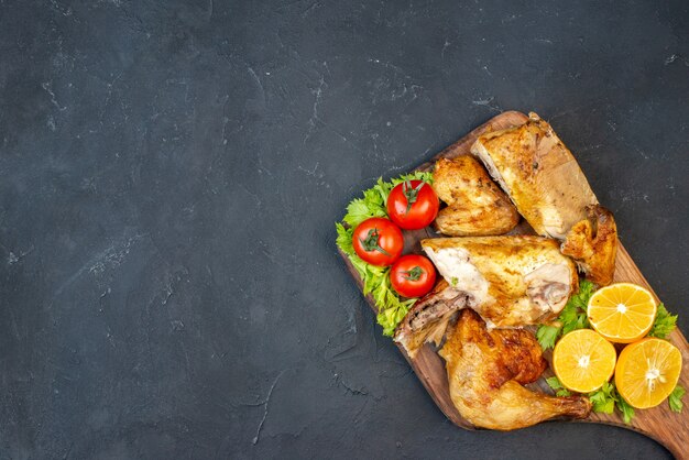 Vista dall'alto pollo al forno pomodori fette di limone su tavola di legno su nero