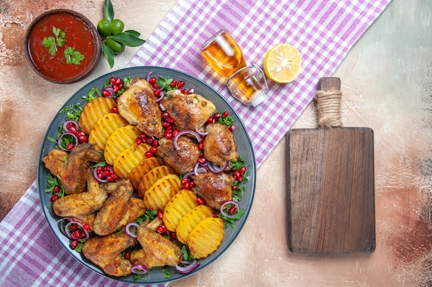 Vista dall'alto pollo ali di pollo patate limone olio sulla tovaglia accanto al tagliere