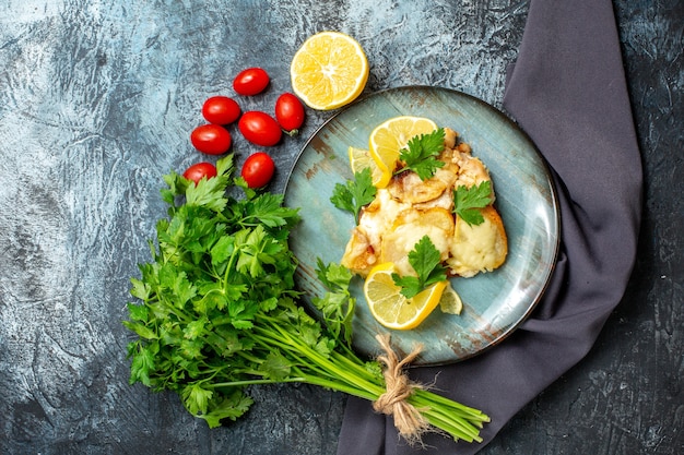 Vista dall'alto pollo con formaggio sul piatto mazzo di prezzemolo mezzo limone pomodorini sul tavolo grigio