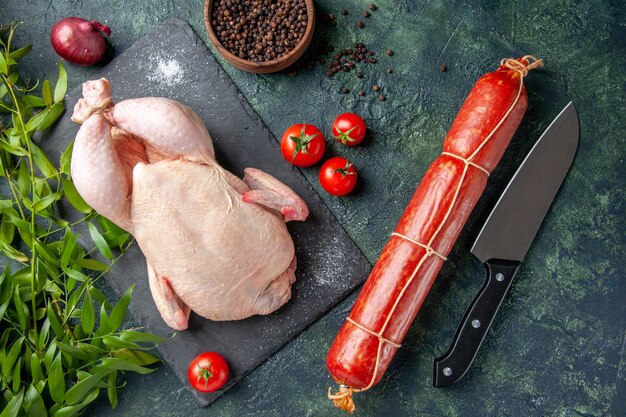 Vista dall'alto pollo crudo fresco con pomodori rossi e salsiccia su sfondo scuro pasto foto animale colore alimentare pollo carne da cucina