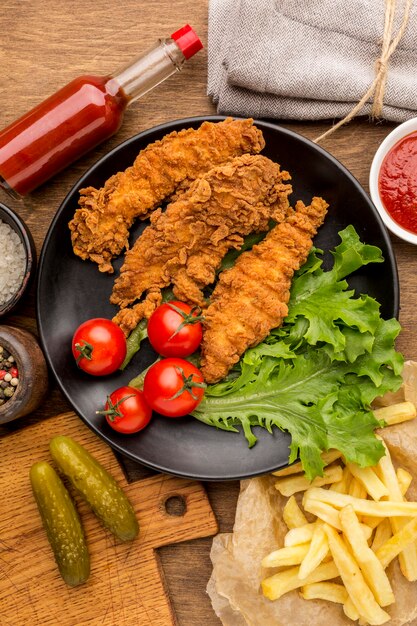 Vista dall'alto pollo fritto con pomodori e insalata sul piatto con patatine fritte