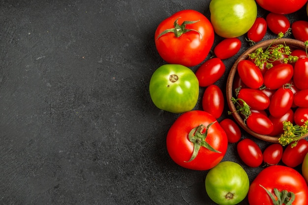 Vista dall'alto pomodori rossi e verdi ciliegia intorno a una ciotola con pomodorini e fiori di aneto sulla destra del terreno scuro con spazio libero