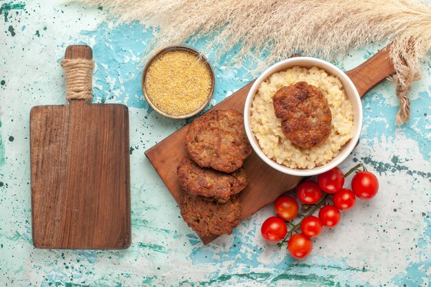 Vista dall'alto pomodorini rossi con cotolette di carne sulla superficie azzurra