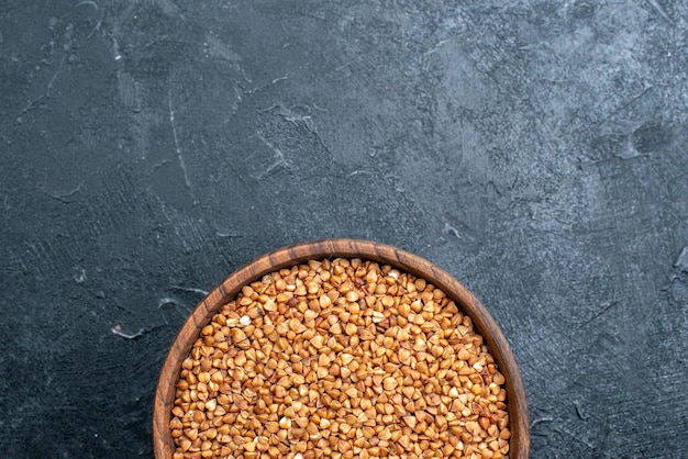 Vista dall'alto prodotto utile di grano saraceno crudo all'interno del piatto nello spazio buio