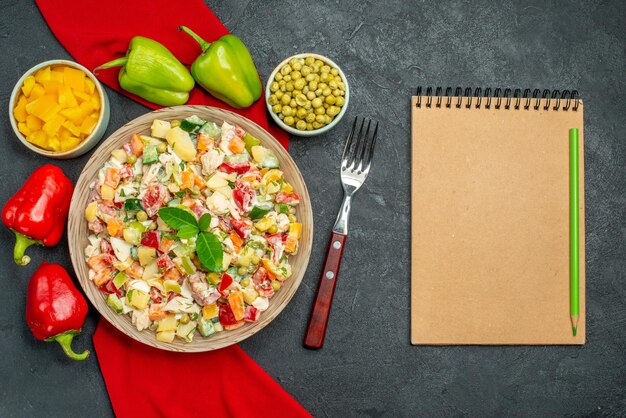 Vista dall'alto ravvicinata di insalata di verdure su tovagliolo rosso con blocco note di verdure e forchetta sul lato su sfondo grigio scuro