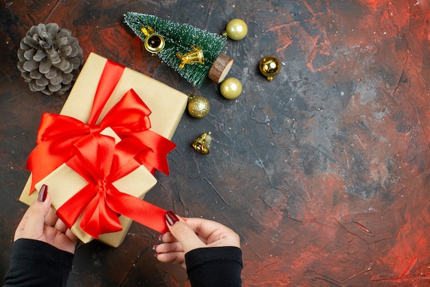 Vista dall'alto regali di natale in mani femminili palline di natale dorate mini albero di natale su spazio copia tavolo rosso scuro