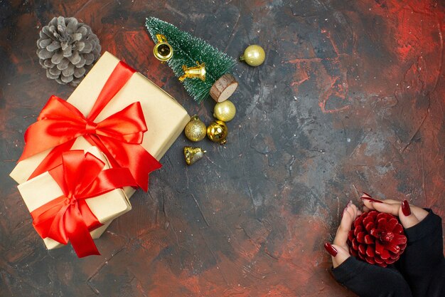 Vista dall'alto regali di natale palle di natale dorate regalo nelle mani della donna sullo spazio della copia del tavolo rosso scuro