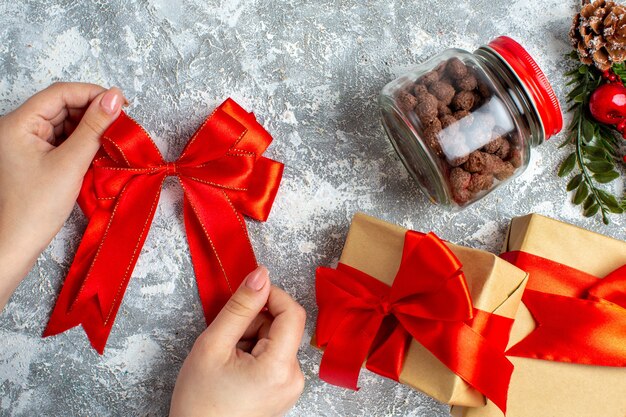 Vista dall'alto regali di natale rosso bowin cereali a mano femminile in barattolo sul tavolo grigio