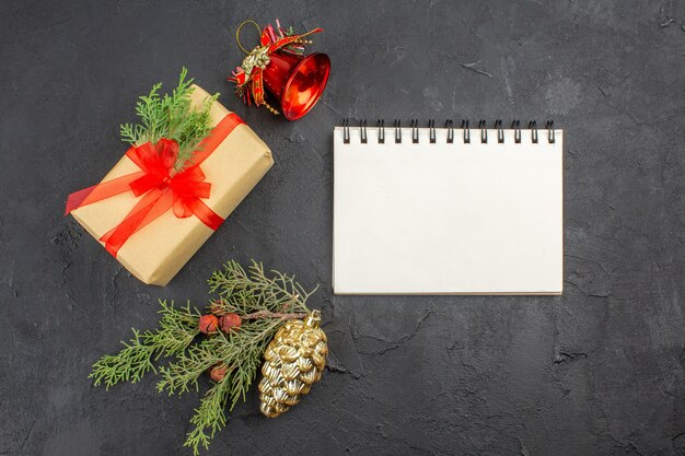 Vista dall'alto regalo di natale in carta marrone legato con nastro rosso ornamenti per alberi di natale quaderno su superficie scura