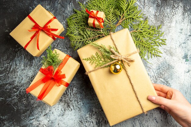 Vista dall'alto regalo di natale in mano femminile piccoli regali rami di pino su superficie grigia