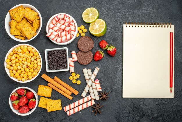 Vista dall'alto ricetta snack panatable con limone fresco e fragole vicino alla penna del taccuino in bianco sulla superficie nera con spazio libero