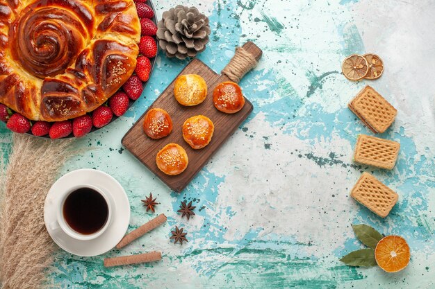 Vista dall'alto rotonda deliziosa torta con cialde di fragole e tazza di tè sulla superficie azzurra