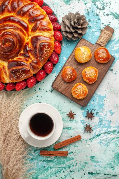 Vista dall'alto rotonda deliziosa torta con torte di fragole rosse fresche e tazza di tè sulla superficie azzurra