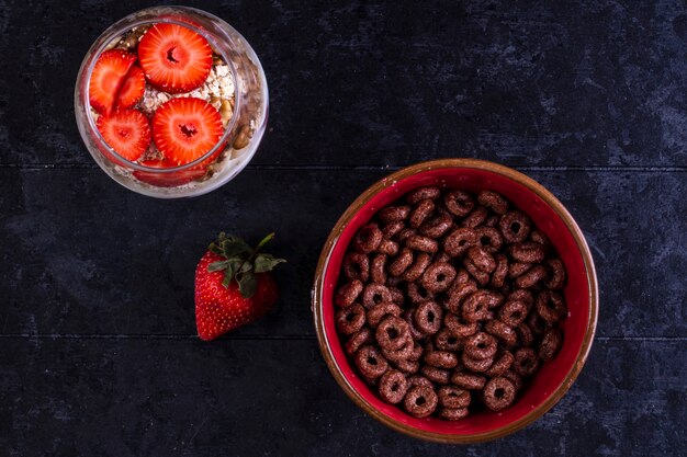 vista dall'alto scaglie di cioccolato in una ciotola con muesli in un bicchiere con frutta e fragole