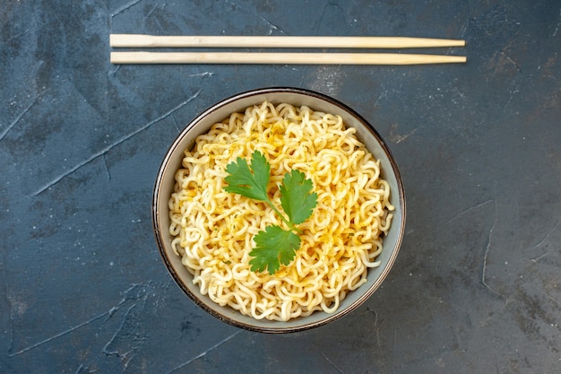 Vista dall'alto spaghetti ramen asiatici con coriandolo in bacchette ciotola sul tavolo scuro