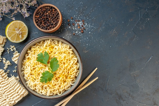 Vista dall'alto spaghetti ramen asiatici in una ciotola pepe nero in una piccola ciotola bacchette di limone tagliate su un tavolo scuro