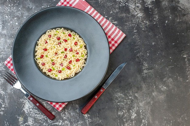 Vista dall'alto spaghetti ramen asiatici su piatto tondo scuro tovagliolo a scacchi bianco rosso una forchetta e coltello su sfondo scuro