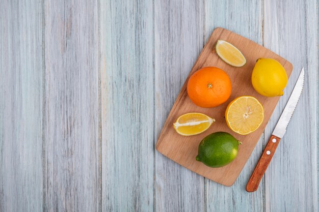 Vista dall'alto spazio copia arancione con limone e lime sul tagliere con coltello su sfondo grigio