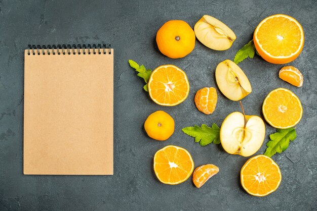 Vista dall'alto tagliare arance e mele un quaderno su una superficie scura