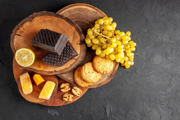 Vista dall'alto tavole di legno tagliate al limone pezzi di biscotti al cioccolato fondente uva su sfondo scuro