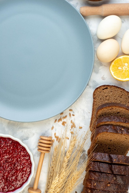 Vista dall'alto tavolo per la colazione con piatto blu uova marmellata gelatina pane scuro su sfondo bianco pasta per caffè torta forno tè del mattino uova panino