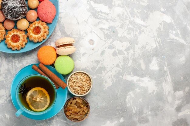 Vista dall'alto tazza di tè con biscotti di zucchero macarons francesi e torte su superficie bianca