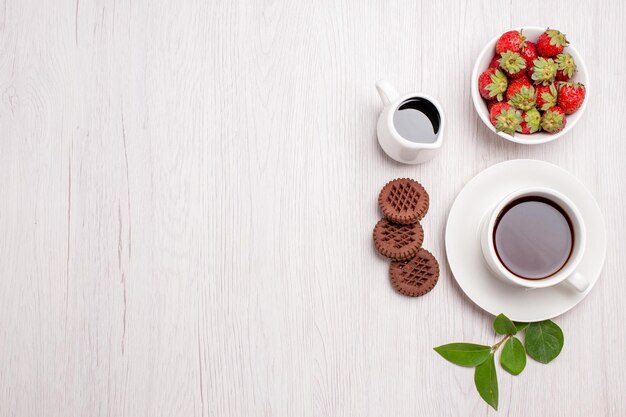 Vista dall'alto tazza di tè con biscotti e fragole su scrivania bianca zucchero tè biscotti biscotti dolci