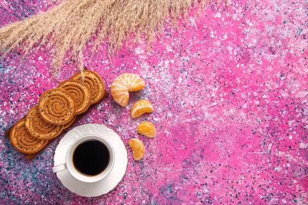 Vista dall'alto tazza di tè con biscotti e mandarini sulla scrivania rosa chiaro.