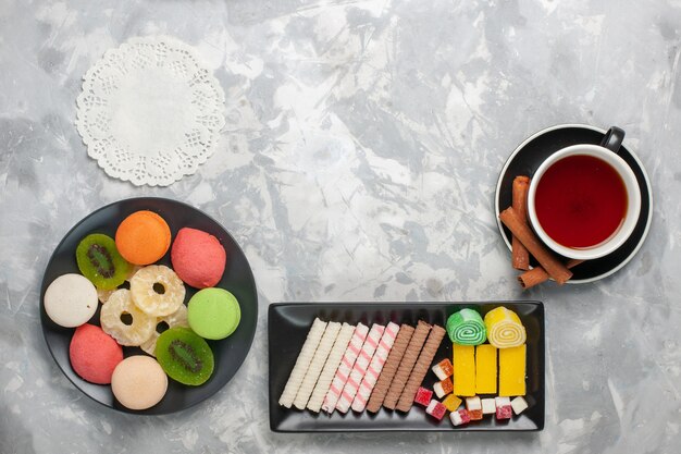 Vista dall'alto tazza di tè con biscotti e piccole torte colorate su superficie bianca