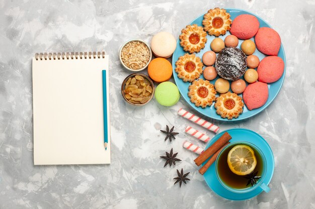 Vista dall'alto tazza di tè con biscotti e torte macarons francesi sulla superficie bianca