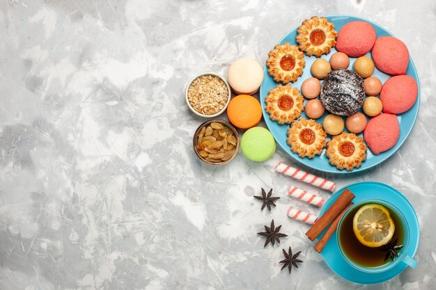 Vista dall'alto tazza di tè con biscotti e torte macarons sulla scrivania bianca