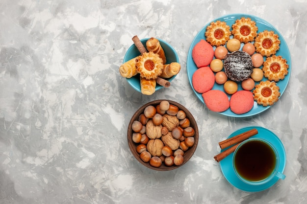 Vista dall'alto tazza di tè con biscotti torte e noci su superficie bianca