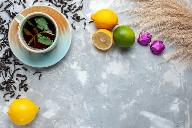 Vista dall'alto tazza di tè con caramelle di chicchi di tè essiccati freschi e limone sul tavolo luminoso, colazione da bere tè