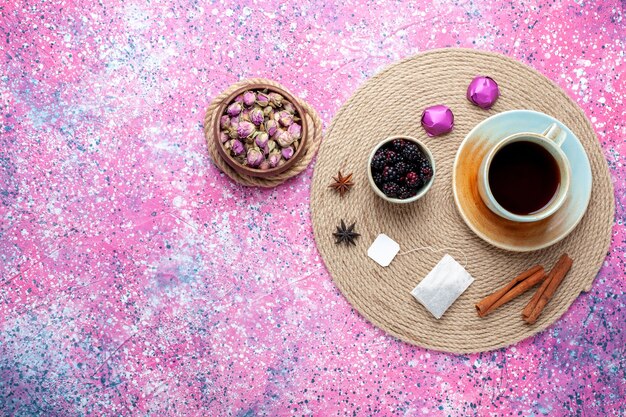 Vista dall'alto tazza di tè con caramelle e cannella su sfondo rosa.