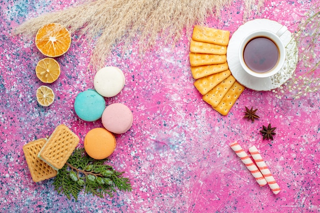 Vista dall'alto tazza di tè con cracker e macarons francesi sulla scrivania rosa chiaro