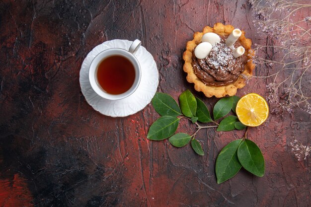 Vista dall'alto tazza di tè con deliziosa piccola torta su un biscotto dessert biscotto tavolo scuro