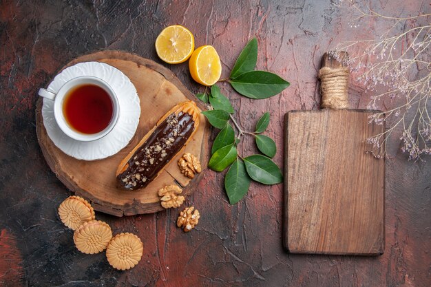 Vista dall'alto tazza di tè con eclair e biscotti sulla torta biscotto dolce tavolo scuro