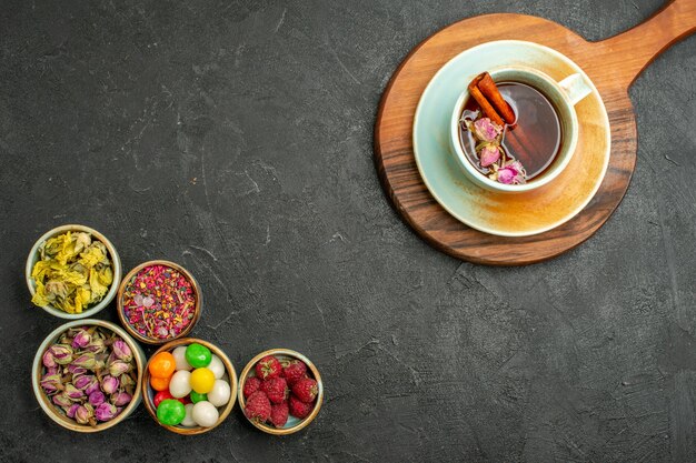 Vista dall'alto tazza di tè con fiori e caramelle sullo spazio grigio