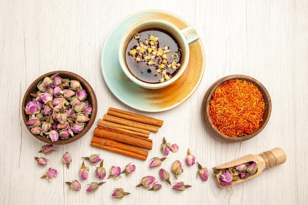 Vista dall'alto tazza di tè con fiori secchi e cannella sul fiore di colore del tè da scrivania bianco