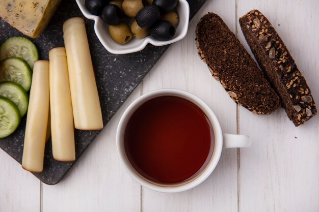 Vista dall'alto tazza di tè con formaggi affumicati con olive e fette di pane nero su sfondo bianco